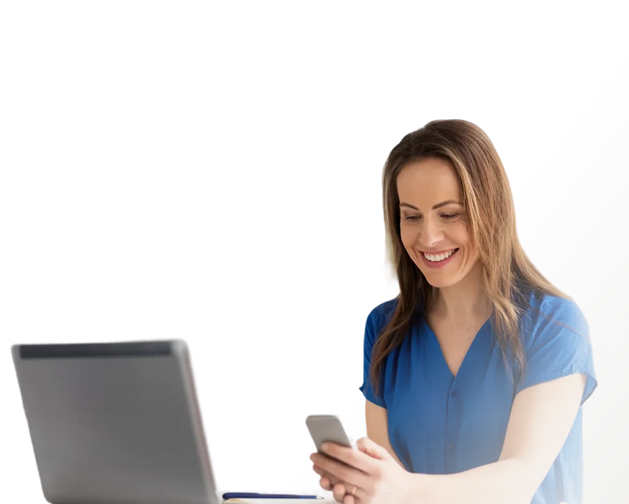 Smiling woman in blue blouse using smartphone with an open laptop in front of her.